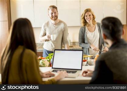 Happy group of young men and women cooking together at home in modern kitchen