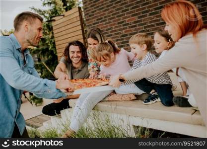 Happy group of young people and kids eating pizza in the house backyard
