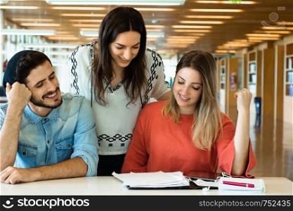 Happy group of young students studying together in university library. Young people are spending time together.