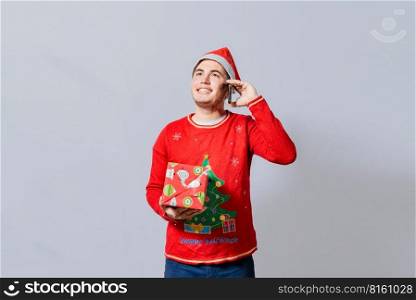 Happy guy holding gift and calling family at christmas, Smiling guy in christmas hat holding christmas gift box and talking on the phone, Christmas man holding gift and calling family on phone
