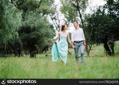 happy guy in a white shirt and a girl in a turquoise dress, the bride and groom are walking in the forest park