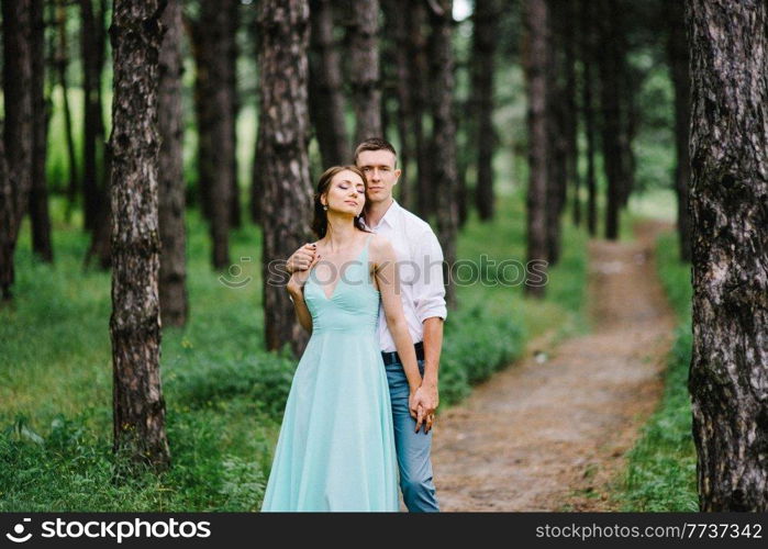 happy guy in a white shirt and a girl in a turquoise dress, the bride and groom are walking in the forest park