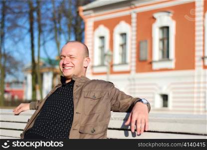 happy guy is sitting on the bench in an autumn city park