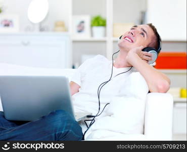 happy guy listening music in headphone from laptop and lying on the sofa