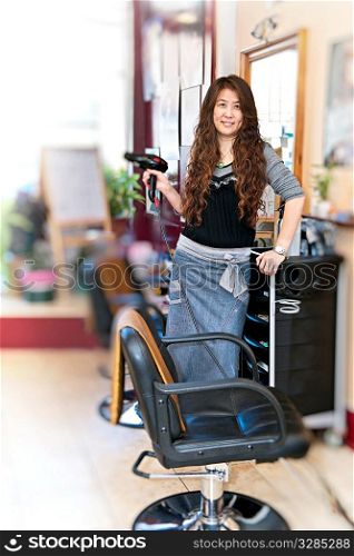 Happy hairdresser holding hairdryer in hair salon