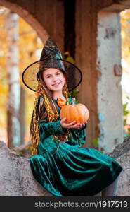 Happy halloween celebration. Beautiful girl witch with pumpkin in the park, outdoors. Little girl in halloween costume with jack pumpkin.. Happy halloween celebration. Beautiful girl witch with pumpkin in the park, outdoors.