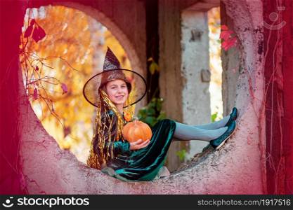 Happy halloween celebration. Beautiful girl witch with pumpkin in the park, outdoors. Little girl in halloween costume with jack pumpkin.. Happy halloween celebration. Beautiful girl witch with pumpkin in the park, outdoors.