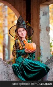 Happy halloween celebration. Beautiful girl witch with pumpkin in the park, outdoors. Little girl in halloween costume with jack pumpkin.. Happy halloween celebration. Beautiful girl witch with pumpkin in the park, outdoors.