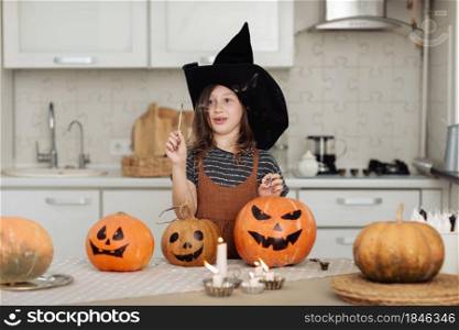 Happy halloween. Cute little girl in witch costume with carving pumpkin. Happy family preparing for Halloween. girl lights candles.. Happy halloween. Cute little girl in witch costume with carving pumpkin. Happy family preparing for Halloween. girl lights candles