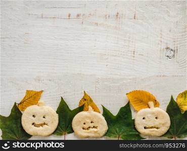 Happy Halloween. Fragrant, fresh cookies in the shape of a pumpkin, yellow and green leaves, lying on a white board. Top view, close-up. Congratulations to loved ones, relatives, friends, colleagues. Cookies in the shape of a pumpkin