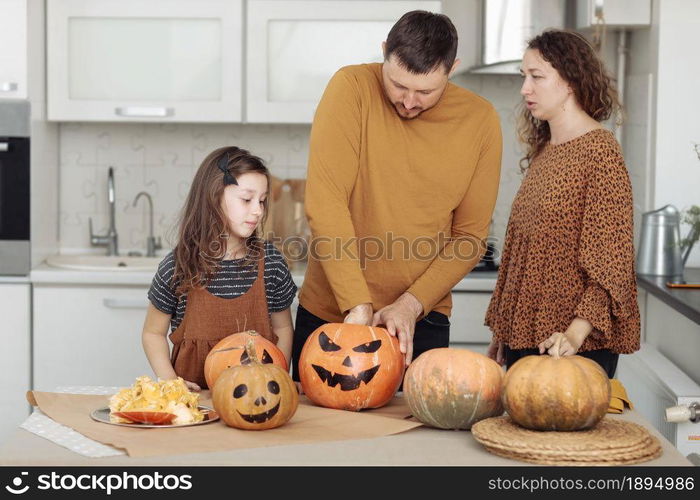 Happy Halloween. Mother, father and their daughter carve a pumpkin. Happy family is preparing for Halloween.. Happy Halloween. Mother, father and their daughter carve a pumpkin. Happy family is preparing for Halloween