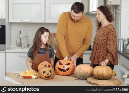 Happy Halloween. Mother, father and their daughter carve a pumpkin. Happy family is preparing for Halloween.. Happy Halloween. Mother, father and their daughter carve a pumpkin. Happy family is preparing for Halloween