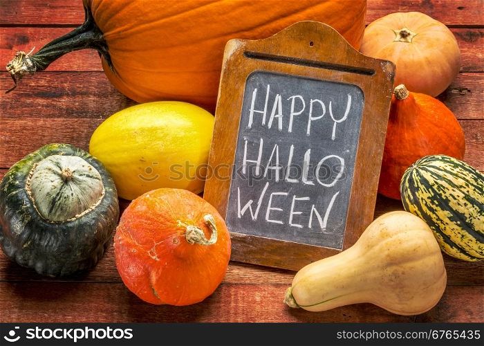 Happy Halloween - white chalk handwriting on a small blackboard surrounded by pumpkin and winter squash