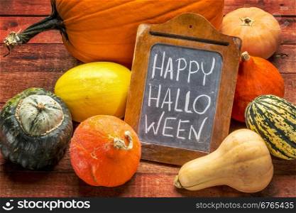 Happy Halloween - white chalk handwriting on a small blackboard surrounded by pumpkin and winter squash