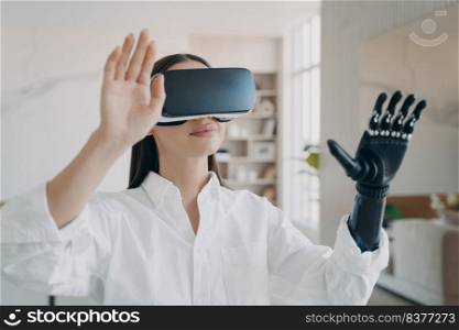 Happy handicapped girl in vr glasses at home. Disabled person gets rehabilitation. Young european woman with artificial hand is excited with 3d cyber vision. Amputee has modern bionic limb.. Happy handicapped girl in vr glasses at home. Woman with artificial hand is excited with 3d vision.
