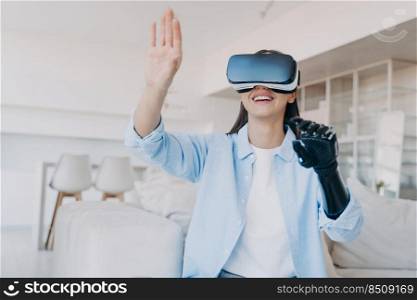 Happy handicapped girl in vr glasses. Disabled person gets rehabilitation in cyber space. Young caucasian woman sitting in living room on couch touches the vision. Amputee with bionic limb prosthesis.. Handicapped girl gets rehabilitation in vr glasses. Amputee with bionic limb prosthesis.