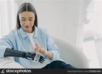 Happy handicapped girl is setting up her artificial limb and pressing buttons. Young european woman with cyber hand at home. Modern robotic bionic prosthesis and orthopedic technology. Copy space.. Happy handicapped girl is setting up her artificial limb and pressing buttons. Copy space.