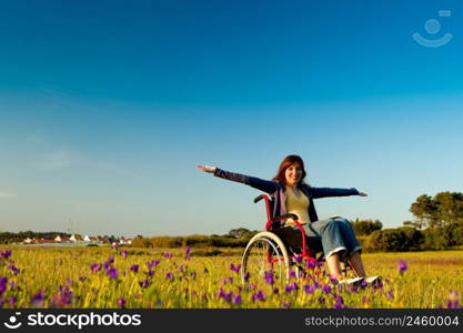 Happy handicapped woman on a wheelchair over a green meadow 