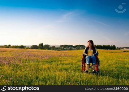 Happy handicapped woman on a wheelchair over a green meadow looking away