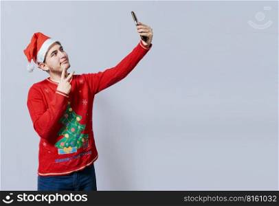 Happy handsome man in christmas hat taking a selfie. Happy guy taking a christmas selfie on isolated background, Smiling young man in christmas hat taking a selfie isolated