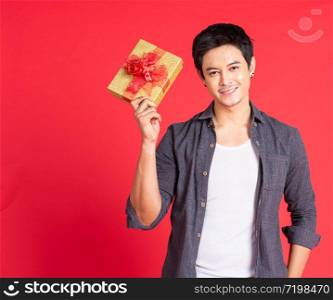 Happy handsome young asian man giving Christmas gift isolated on red background in studio shot.