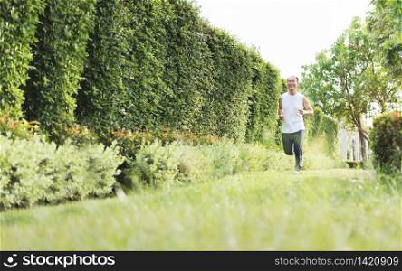 Happy Healthy Asian Senior man enjoying workout at outdoor with copy space. Portrait of Smiling Elderly male jogging exercise at the park. Health, Lifestyle, Wellness.