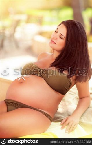 Happy healthy pregnant woman on summer vacation, relaxing on the beach with drawing sun on the tummy, using sunscreen for skin protection