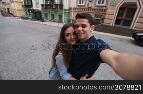 Happy hipster couple in love taking self portrait witn smartphone while enjoying time together in city streets during travel on vacation. Attractive couple making selfie on smartphone outdoors.