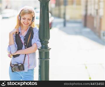 Happy hipster girl listening music on city street