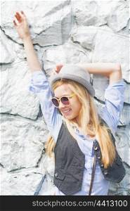 Happy hipster girl posing against rocky wall outdoors