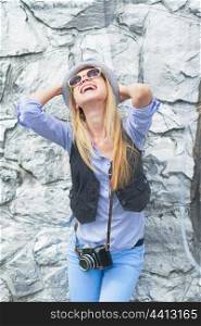 Happy hipster girl rejoicing against rocky wall outdoors