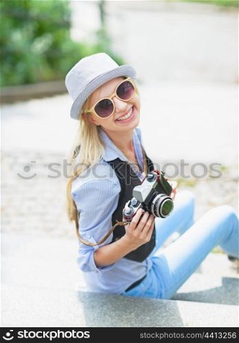 Happy hipster girl sitting on stairs with retro photo camera