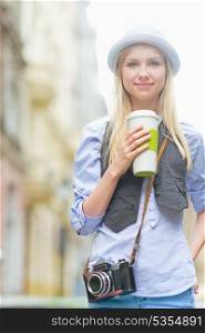 Happy hipster girl with cup of hot beverage on city street