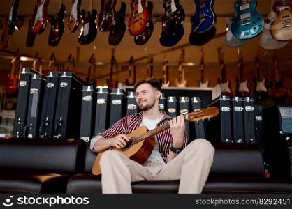 Happy hipster man musician smiling and playing electric guitar over string instrument shop store background. Happy man musician playing guitar over string instrument shop store background