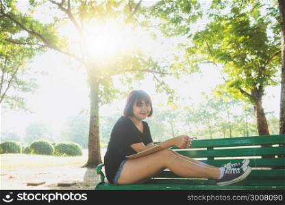 Happy hipster young asian woman writing into her diary in park. Happy hipster young asian woman working on notebook in park. Student studying outdoors. Lifestyle woman outdoor concept. Flare light.