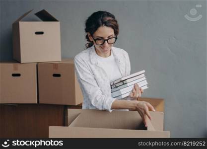 Happy hispanic female packing items into cardboard box on relocation day. Smiling female homeowner tenant in glasses gathering belongings, preparing to move to new dwelling. Moving and repair concept.. Hispanic female packing items in carton box on relocation day. Moving, renovation, mortgage concept
