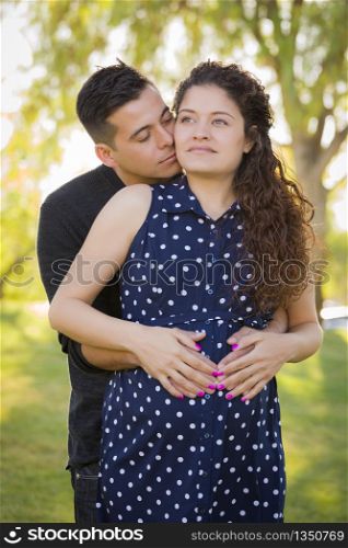 Happy Hispanic Man Hugs His Pregnant Wife Outdoors At The Park.