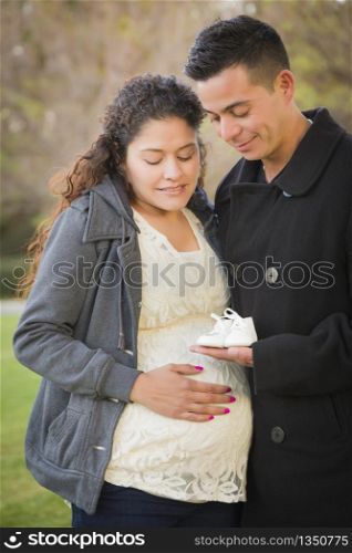 Happy Hispanic Pregnant Couple Holding Baby Shoes Outside in the Park.
