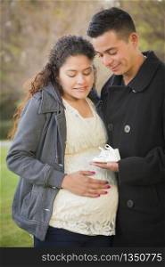 Happy Hispanic Pregnant Couple Holding Baby Shoes Outside in the Park.