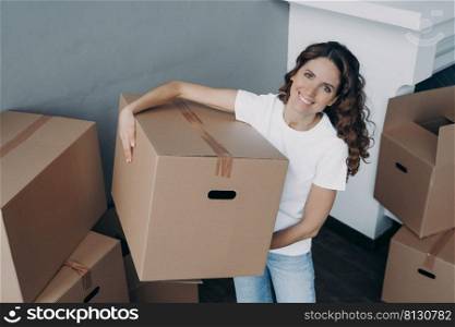 Happy hispanic woman purchasing real estate and carrying box. Lady is unloading cardboard boxes alone in new apartment. Young lady is going to rent house. Mortgage loan and investment concept.. Happy hispanic woman purchasing real estate and unloading cardboard boxes alone in new apartment.