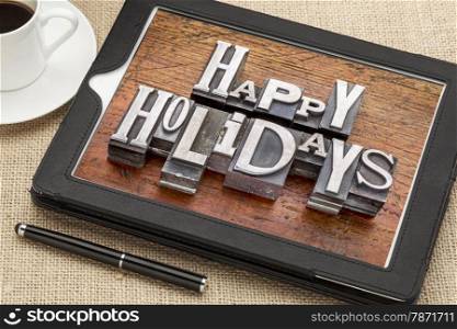 Happy Holidays greetings in vintage metal type printing blocks on a digital tablet with a cup of coffee
