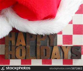 happy holidays in old wood type on a checkerboard with a furry Santa hat