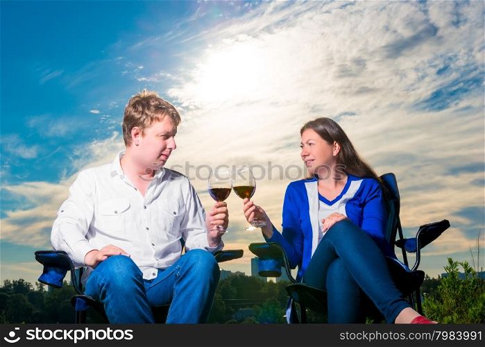 happy husband and wife with glasses on chairs at sunset
