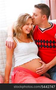 Happy husband kissing pregnant wife and holding her belly&#xA;