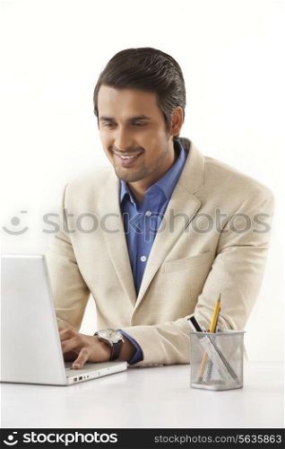 Happy Indian businessman in suit using laptop at office desk