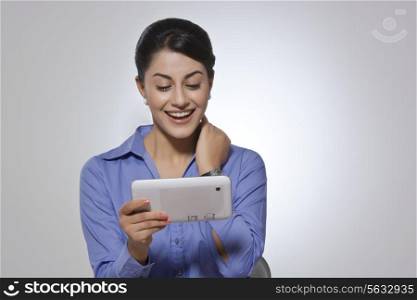 Happy Indian businesswoman using digital tablet against gray background