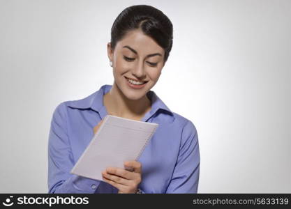 Happy Indian businesswoman writing on notebook against gray background
