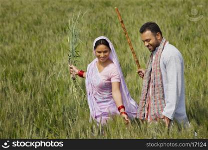 Happy Indian couple gliding through wheat field