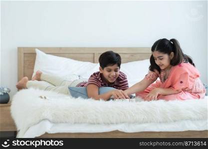 Happy Indian family brother and sister playing fun game together, boy lying and girl with traditional clothes sitting on bed at home, sibling relationship concept