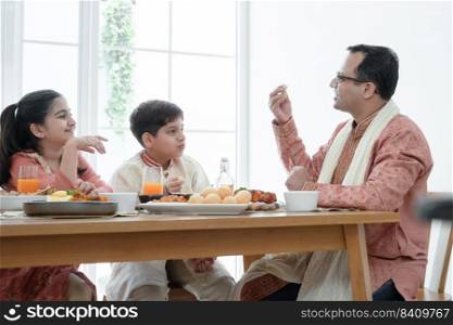 Happy Indian family enjoy eating food with hands, South Asian father and children wear traditional clothes, sitting and talking at dining table at home together. Indian culture lifestyle